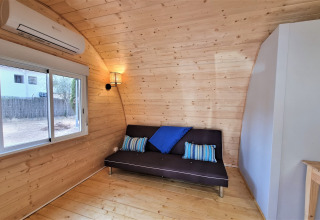 Interior view of Nomad Paraiso pod in Spain featuring wood walls, black sofa and blue cushions.