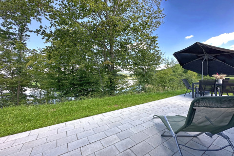 Vista dal patio al Holiday Village SEEBLICK, Tiny Chalet am Eixendorfer See con alberi e lago in Germania.