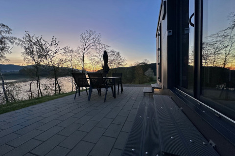 Terras van tiny house met stoelen en tafel, zicht op meer en heuvels bij zonsondergang in Duitsland.