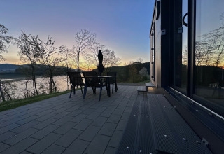 Terrasse ved tiny house med bord og stole, udsigt over sø og bakker ved solnedgang i Tyskland.