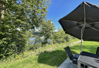 Terraszicht bij SEEBLICK - Tiny Chalet am Eixendorfer See met parasol, stoelen en tafel aan het meer.