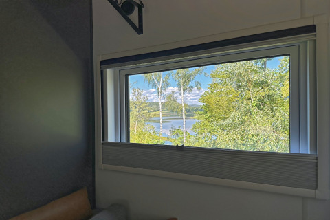 Uitzicht vanuit een tiny house-raam op groene bomen en het meer Eixendorfer See in Duitsland bij zonnig weer.