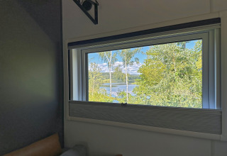 Vue depuis la fenêtre d’une tiny house sur des arbres verts et le lac Eixendorfer See, en Allemagne, ensoleillé.