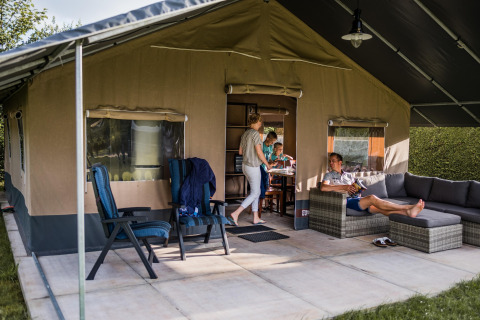 Une famille se détend devant une tente safari avec canapé, chaises et coin repas extérieur.