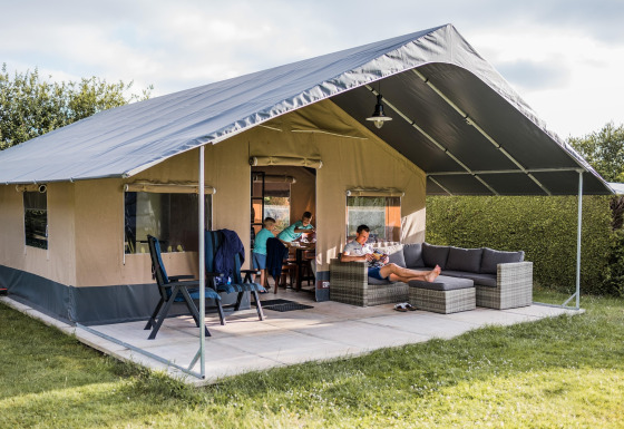 Tente safari Resort Begur 3, famille détendue sur la terrasse, mobilier confortable et cadre verdoyant.