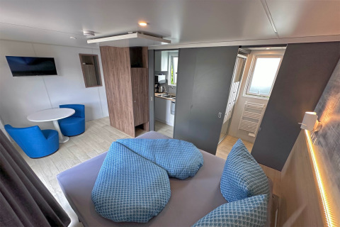 Interior of a modern tiny house at Holiday village SEEBLICK, showing bed, kitchen and sitting area.