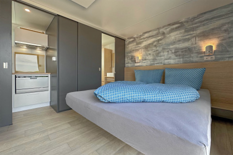 Chambre moderne avec lit double, literie bleue, petite cuisine et appliques murales dans tiny house.