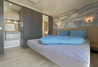 Moderne soveværelse med dobbeltseng, blå sengetøj, lille køkken og elegante væglys i et tiny house.