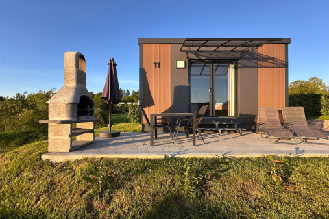 Casa pequeña moderna con terraza, barbacoa, muebles de jardín y tumbonas en aldea vacacional en Alemania.