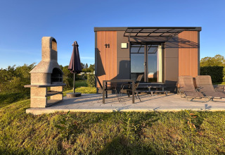 Modern tiny house with patio, BBQ, garden furniture, and sun loungers in a sunny holiday village in Germany.