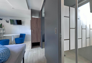 Interno moderno di tiny house con letto, area salotto, TV, tavolo e doccia con vetri smerigliati in Germania.