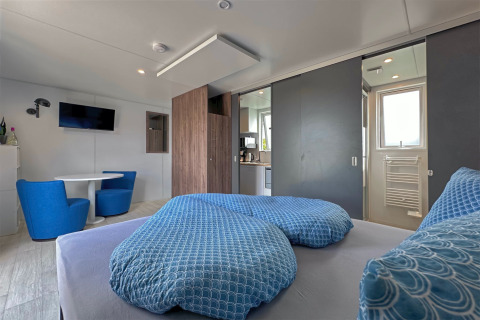 Moderne, kompakt tiny house med blå sengetøj, spiseområde og køkken ved Eixendorfer See, Tyskland.