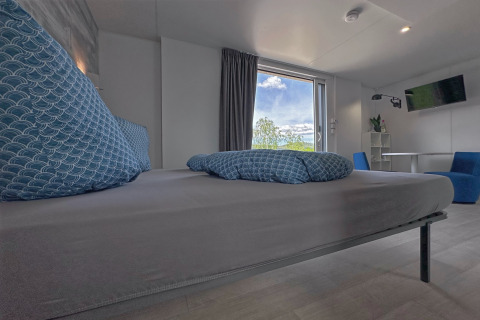 Chambre moderne avec grands coussins bleus, vue par la fenêtre et déco minimaliste dans une tiny house.