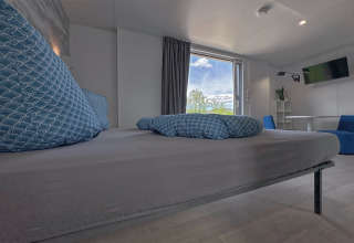 Modern bedroom in a tiny house with large blue pillows, window view, and minimalist decor in Germany.