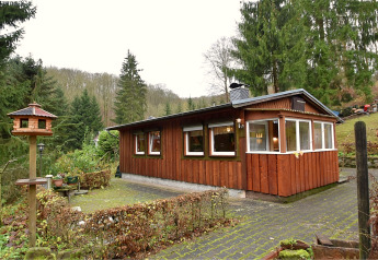 Photo of a lodge named Neustadt, surrounded by forest with a birdhouse and garden in the foreground.