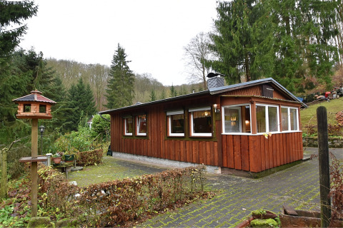 Foto van een lodge genaamd Neustadt, omringd door bos met een vogelhuisje en tuin op de voorgrond.