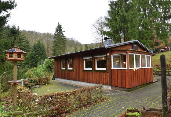 Foto van een lodge genaamd Neustadt, omringd door bos met een vogelhuisje en tuin op de voorgrond.