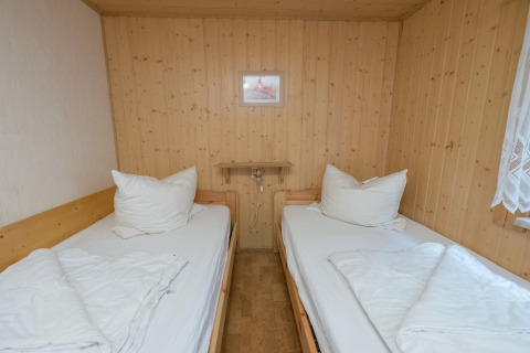 Twee eenpersoonsbedden met wit beddengoed in een knusse houten kamer van de Neustadt-lodge in Duitsland.