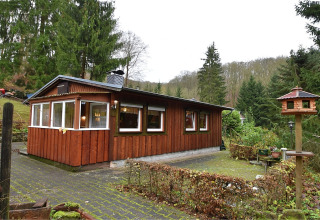 Houten lodge genaamd Neustadt in Duitsland, omgeven door groene bomen, buitenaanzicht overdag.