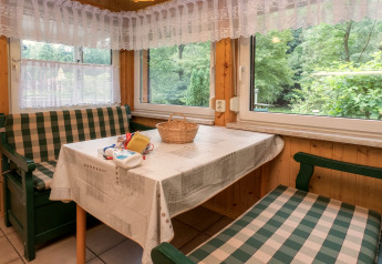 Cozy dining nook at lodge Neustadt in Germany, with plaid benches, tablecloth, and forest view.