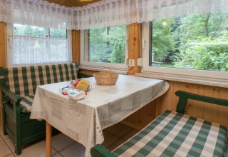 Gezellige eethoek in lodge Neustadt in Duitsland, met geruite banken, tafelkleed en bosuitzicht.