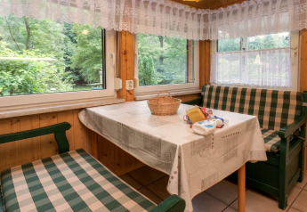 Cozy dining nook in Neustadt lodge, Germany, with checkered benches, lace curtains, and woodland view.