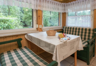 Knusse eethoek in lodge Neustadt, Duitsland met geruite banken, witte tafelkleed en uitzicht op het bos.