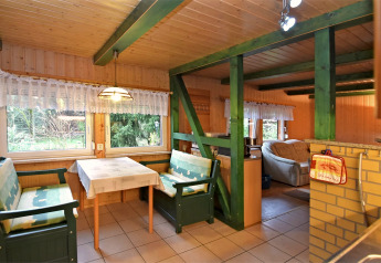 Dining area inside the lodge 'Neustadt' in Germany, with green benches, lace curtains, and wood interior.
