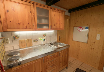 Small wood-paneled kitchen in Neustadt lodge in Germany with stovetop and metal sink.
