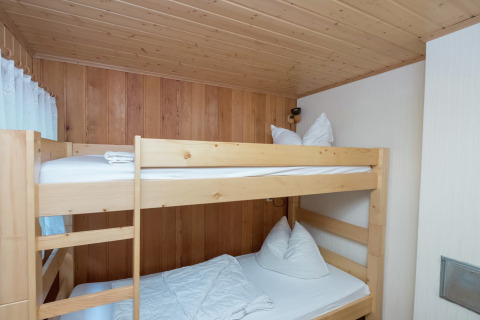 Kamer met houten stapelbed, wit beddengoed en houten panelen in de Neustadt-lodge in Duitsland.