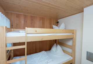 Kamer met houten stapelbed, wit beddengoed en houten panelen in de Neustadt-lodge in Duitsland.