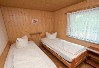 Bedroom with two single beds, wooden walls, and a large window at Neustadt lodge in Germany.