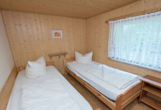 Slaapkamer met twee eenpersoonsbedden, houten wanden en groot raam in lodge Neustadt in Duitsland.