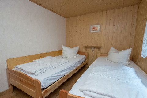 Kamer met twee eenpersoonsbedden, houten betimmering en wit beddengoed in lodge 'Neustadt' in Duitsland.