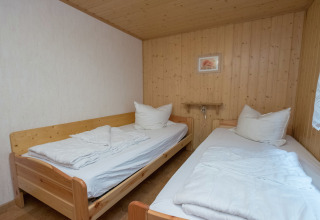Kamer met twee eenpersoonsbedden, houten betimmering en wit beddengoed in lodge 'Neustadt' in Duitsland.