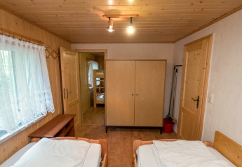 Cozy wooden bedroom at Neustadt lodge with twin beds, wardrobe, and view into a room with bunk beds.