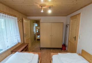 Gezellige houten slaapkamer in lodge Neustadt met twee bedden, kast en zicht op kamer met stapelbedden.