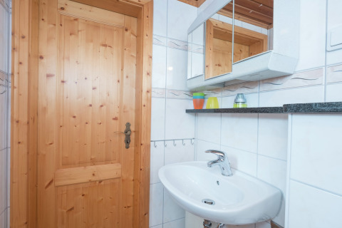 Lichte badkamer in lodge Neustadt in Duitsland met houten deur, spiegelkast en witte wastafel.