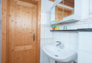 Lichte badkamer in lodge Neustadt in Duitsland met houten deur, spiegelkast en witte wastafel.