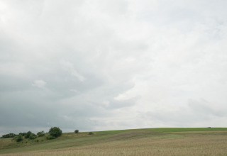 Foto van open velden en glooiende heuvels onder een bewolkte lucht bij een glampingverblijf.