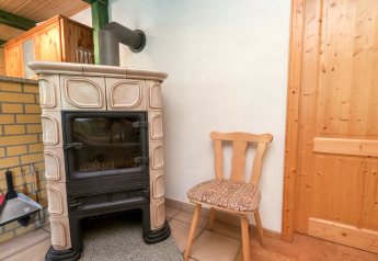 Wooden chair next to a classic fireplace stove in a cozy corner of Lodge Neustadt, Germany.