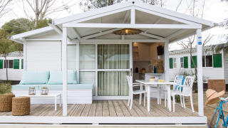 Hvid chalet ved Tamarit Park Resort med overdækket terrasse, havemøbler og hyggelig udendørs siddeplads.