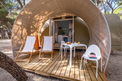 Udendørs terrasse ved en safaritelts indgang med stole, bord og mad på Camping Estival Torre de la Mora i Spanien.