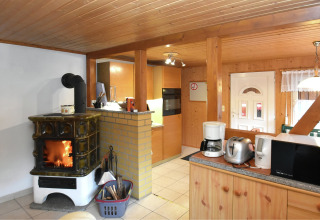 Gemütliches Wohnzimmer in einem Ferienhaus in Deutschland mit Holzofen, Küchengeräten und Holzwänden.