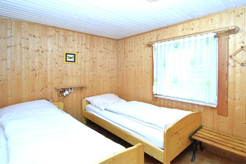 Schlafzimmer im Chalet mit zwei Einzelbetten, Holzvertäfelung, Fenster mit Vorhang und kleinem Bild an der Wand.