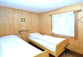 Soveværelse i chalet med to enkeltsenge, træpaneler, et vindue med gardin og et lille billede på væggen.