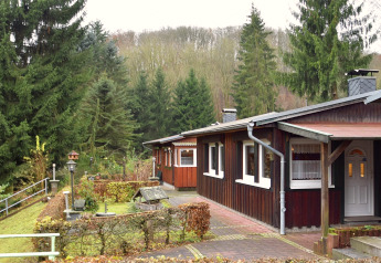 Ferienhaus «with Parking» in Deutschland, aus Holz gebaut, umgeben von Tannen und gepflegtem Garten.