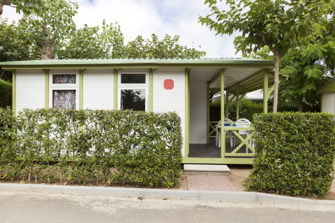 Vista exterior del Camping Cambrils Playa 1 BUNGALOW OASIS con setos verdes, terraza y porche cubierto.
