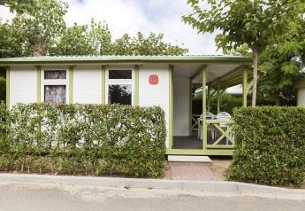 Vista exterior del Camping Cambrils Playa 1 BUNGALOW OASIS con setos verdes, terraza y porche cubierto.
