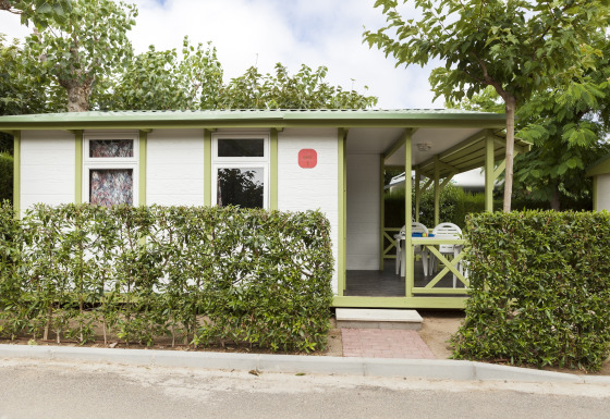 Vista exterior del Camping Cambrils Playa 1 BUNGALOW OASIS con setos verdes, terraza y porche cubierto.